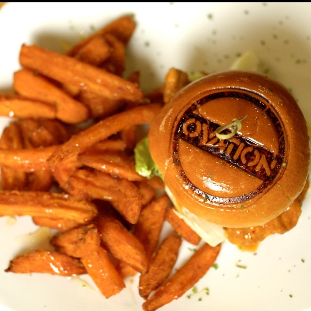 Burger with a burger bun branding iron  'Ovation' and sweet potato fries on a white plate.